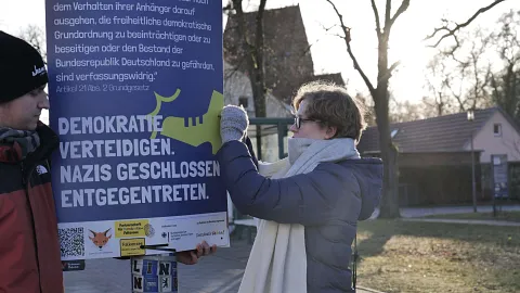 Es wird ein an einem Laternenmast aufgehängt mit der Aufschrift "Demokratie verteidigen. Nazis entschlossen entgegentreten.