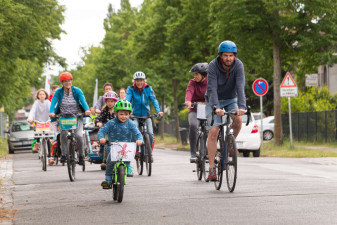 Mehrere junge und ältere Menschen fahren mit dem Fahrrad auf einer Straße mit grünen Bäumen entlang